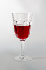 A cup of red wine on an old style looking wine glass with shadow on the right side.