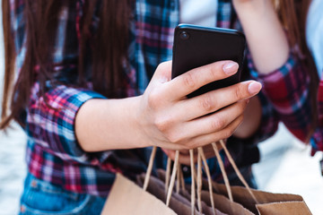 cropped view of girl using smartphone while holding shopping bags