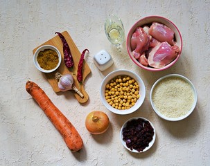 Ingredients for cooking pilaf on a light concrete background: chicken, rice, raisins, carrots, vegetable oil, spices, boiled chickpeas, garlic, hot pepper, salt. Top view. Recipe card.