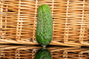 One whole long fresh pickling cucumber with braided rattan behind