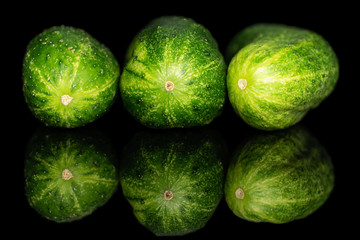 Group of three whole fresh green pickling cucumber in row isolated on black glass
