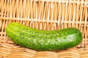 One whole fresh green pickling cucumber with braided rattan behind