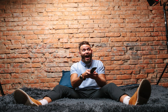 Emotional guy watching football match on television at home. Remote control in hand.