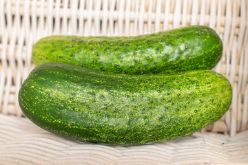 Group of two whole fresh green pickling cucumber with braided rattan behind