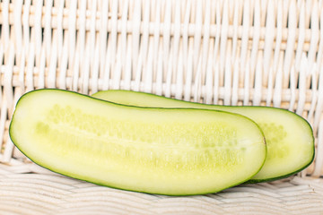 Group of two halves of fresh green pickling cucumber section with braided rattan behind