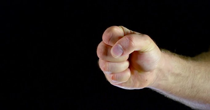 the man clenches his hand into a fist and withdraws it. dark background