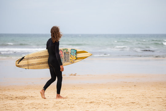 Young man in black wetsuit walking in the beach with surfboard on daytime