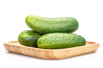 Group of three whole fresh green pickling cucumber on wooden square plate isolated on white background