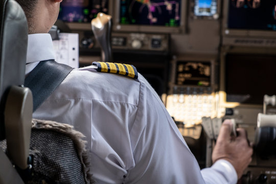Airliner captain controlling airplane in cockpit. He pulling spreed brake lever to slow down the aeroplane speed by right hand. Seen behind pilot seat. Modern aviation concept.