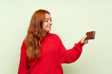 Naklejka premium Teenager redhead girl with sweater over isolated green background holding a wallet