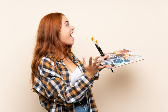 Teenager redhead girl holding a palette over isolated background with surprise facial expression