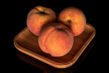 Group of three whole bright fresh fuzzy peach on wooden square plate isolated on black glass