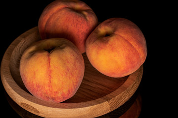 Group of three whole fresh fuzzy peach on bamboo plate isolated on black glass