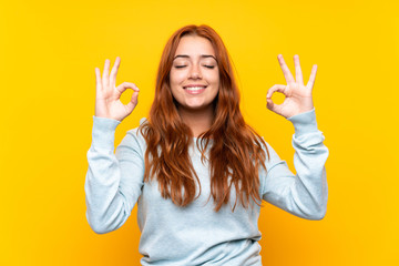 Teenager redhead girl over isolated yellow background in zen pose