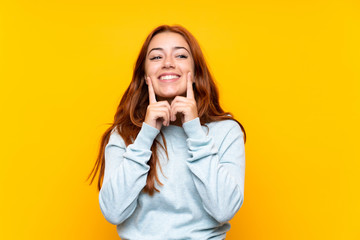Teenager redhead girl over isolated yellow background smiling with a happy and pleasant expression