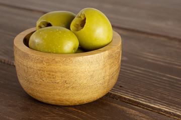 Group of three whole pitted green olive in wooden bowl on brown wood