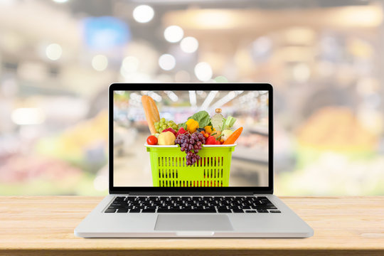 supermarket aisle blurred background with laptop computer and shopping basket on wood table grocery online concept