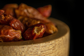 Lot of whole dry red chili pepper peperoncino closeup in wooden bowl isolated on black glass