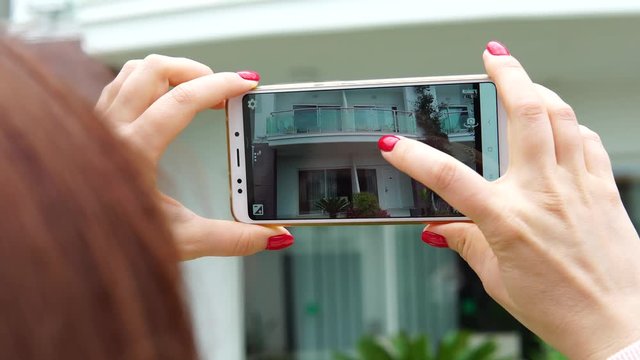 A woman holds a smartphone in her hands and takes pictures of the hotel building. Turkish resort concept.