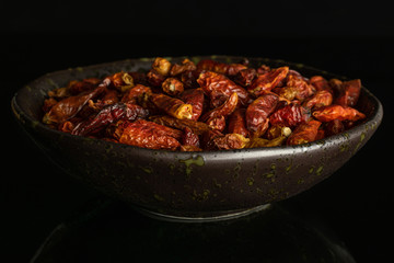 Lot of whole dry red chili pepper peperoncino on grey ceramic plate isolated on black glass