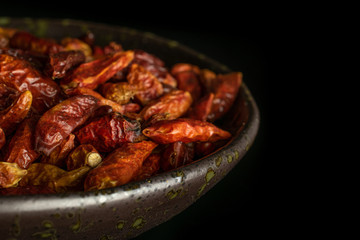 Lot of whole dry red chili pepper peperoncino closeup on grey ceramic plate isolated on black glass