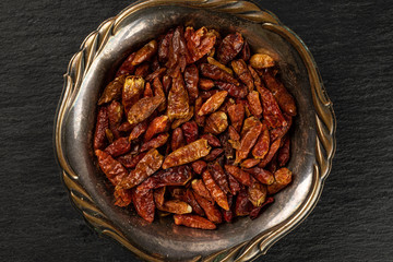 Lot of whole dry red chili pepper peperoncino in old iron bowl flatlay on grey stone