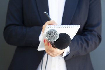 Female journalist at news conference or media event, writing notes, holding microphone