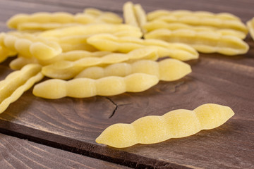 Lot of whole uncooked pasta cavatelli one in focus on brown wood