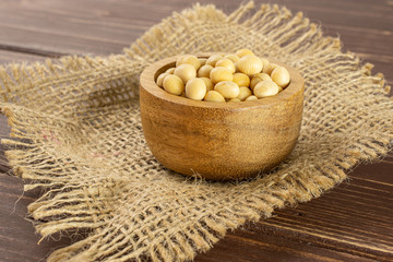 Lot of whole raw yellow soya bean in wooden bowl on jute cloth on brown wood