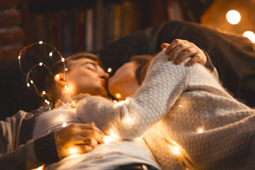 couple in love in a cozy room cuddles among the New Year's garland of lanterns