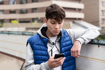 A teenage boy looking into a phone with a sad face and having negative emotions because he read the...