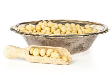 Lot of whole raw yellow soya bean in old iron bowl with wooden scoop isolated on white background