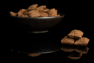 Lot of whole crispy brown cereal pillow in dark ceramic bowl isolated on black glass