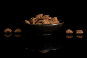 Lot of whole crispy brown cereal pillow in dark ceramic bowl isolated on black glass