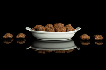 Lot of whole crispy brown cereal pillow in white oval ceramic bowl isolated on black glass