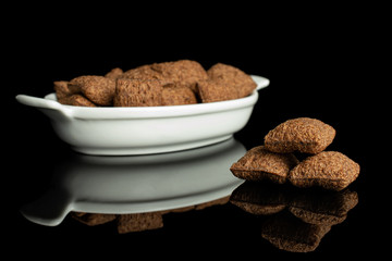 Lot of whole crispy brown cereal pillow in white oval ceramic bowl isolated on black glass