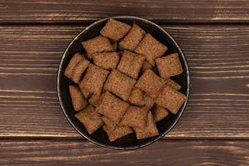 Lot of whole crispy brown cereal pillow in dark ceramic bowl flatlay on brown wood