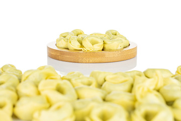 Lot of whole fresh yellow spinach filled tortelloni on bamboo coaster isolated on white background