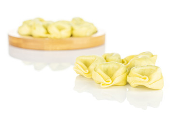 Lot of whole fresh yellow spinach filled tortelloni small group is in the front and the rest is on bamboo coaster isolated on white background