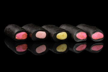 Group of five whole sweet black liquorice candy in row isolated on black glass