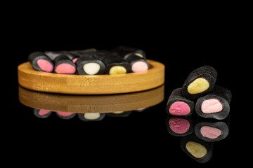 Lot of whole sweet black liquorice candy on bamboo coaster isolated on black glass