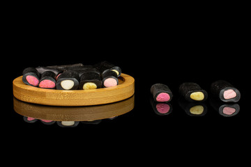 Lot of whole sweet black liquorice candy on bamboo coaster isolated on black glass