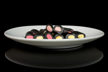 Lot of whole sweet black liquorice candy on white ceramic plate isolated on black glass