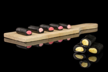 Group of eight whole sweet black liquorice candy on small wooden cutting board isolated on black glass