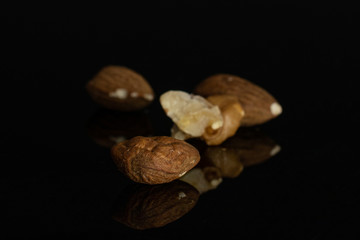 Group of four whole front focus brown almond nut isolated on black glass