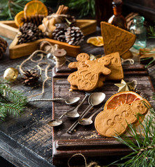 tasty christmas gingerbread cookies on wooden board with vintage spoons on rustic table with christmas tree branches opposite concrete wall, selective focus