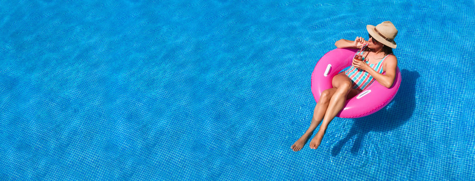 Young Woman With Sunglasses, Hat And Swimsuit In A Blue Pool. Pretty Girl On A Pink Float Enjoying The Summer While Having A Cocktail.