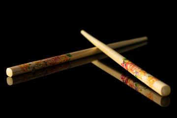 Group of two whole crossed asian brown chopsticks isolated on black glass