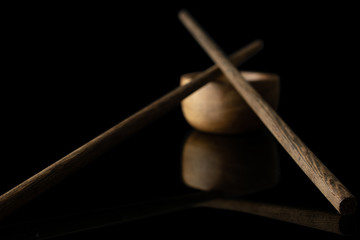 Group of two whole dark asian brown chopsticks crossed with wooden bowl isolated on black glass