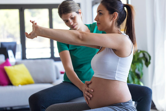 Physiotherapist helping to beautiful pregnant woman for doing pilates exercises with ball preparing for childbirth.